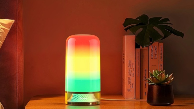 A Govee Smart Table Lamp 2 emitting a soft glow on a bedside table next to books and a plant.