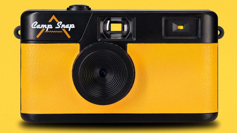 A yellow and black Camp Snap digital camera against a bright yellow background, showing its screen-free back.