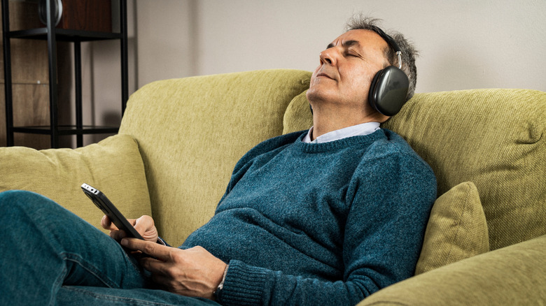 A man relaxing on a sofa while wearing a pair of wireless over-ear headphones.