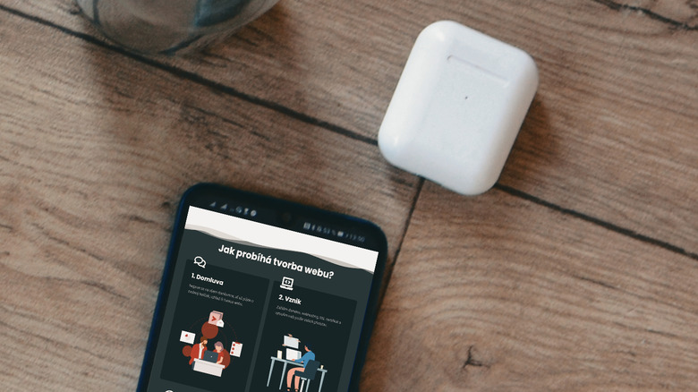 An AirPods case placed on top of a modern Android phone showing a battery widget.