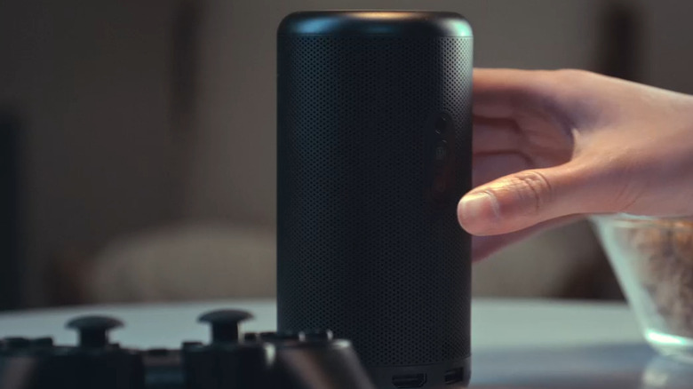 A person's hand picking up the compact Anker Nebula Capsule 3 projector by its handle.