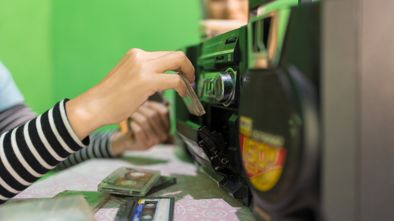 Close-up of a hand inserting a cassette tape into a vintage boombox player.