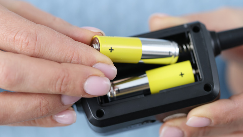 Close-up of hands installing AA batteries into an electronic device.