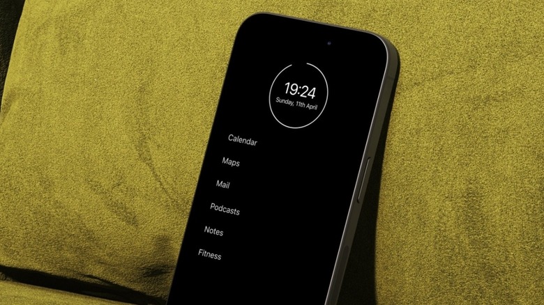 An iPhone running a minimalist text-based home screen interface leaning against a neutral-toned cushion.