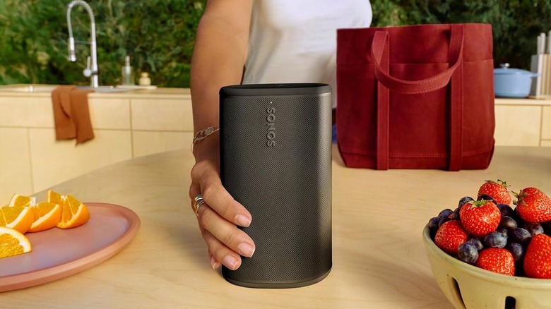 A person placing a Sonos speaker on a modern kitchen countertop.