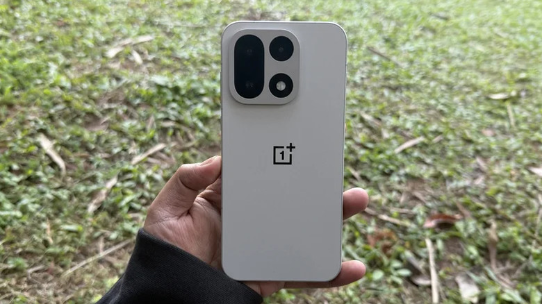 A person holding the OnePlus 15 showing the vibrant screen interface.