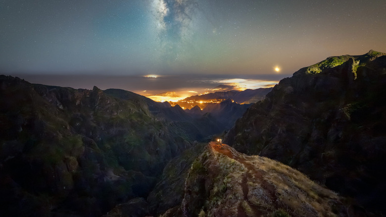 A wide-angle landscape featuring the Milky Way galaxy over dark mountain peaks.