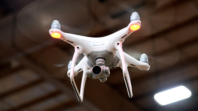 A white DJI Phantom 4 drone flying in the air with its status lights visible.