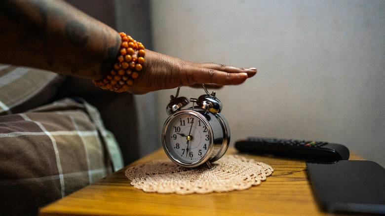 A close-up of a person's hand turning off a traditional twin-bell analog alarm clock.