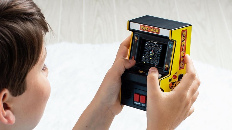 A close-up of a child playing the Arcade Classics Mini Pac-Man handheld console.