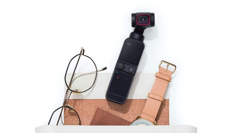 A DJI Pocket 2 gimbal camera on a white surface next to travel accessories.