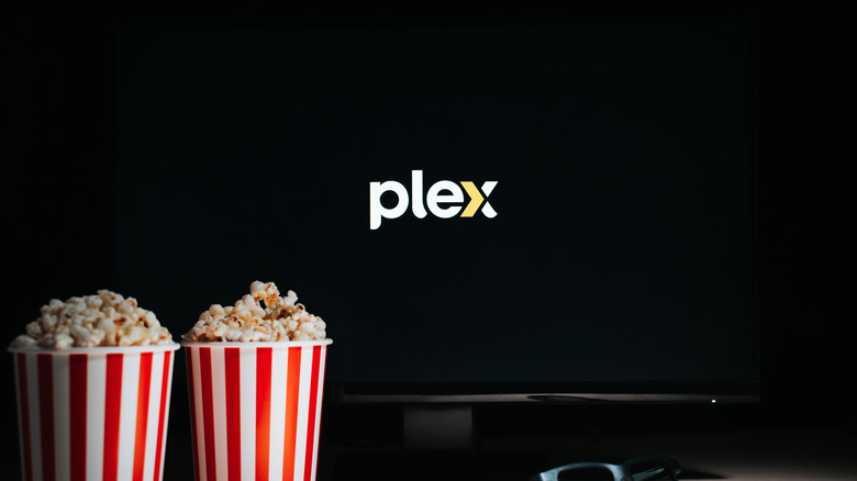 A living room setting with popcorn in focus and the Plex logo visible on the TV screen in the background.