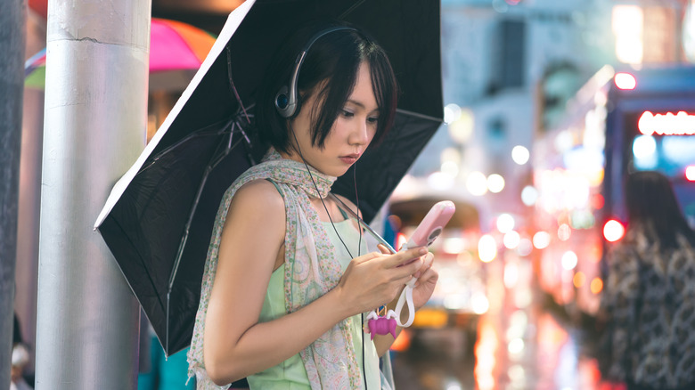 A person using retro-style wired headphones and an old-school pink flip phone.