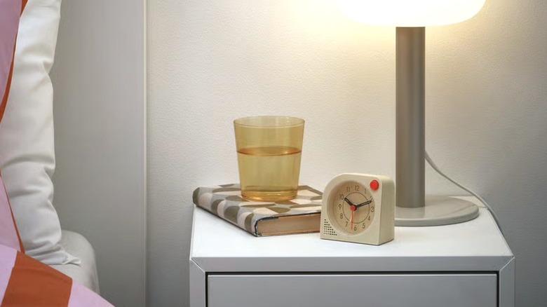 A small, square white Tjinga alarm clock sitting on a bedside nightstand.