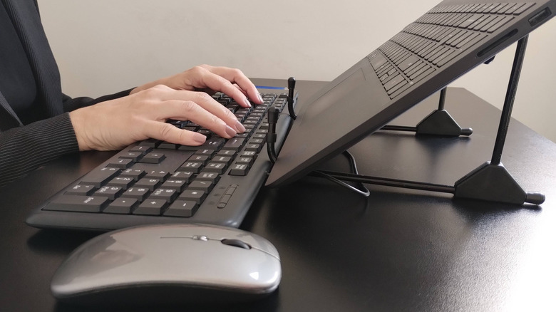 Close up of a person using a laptop with an external mouse and keyboard for better ergonomics.