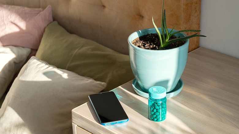 A bottle of green pills next to a smartphone on a wooden surface.
