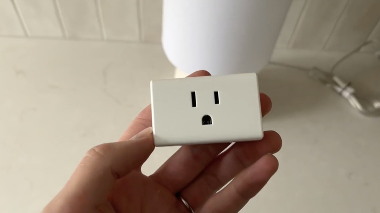 A hand holding a compact smart plug against a white background.