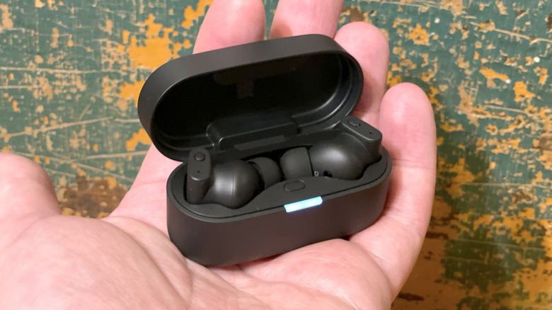 A hand holding the open Status Pro X charging case with the earbuds tucked inside.