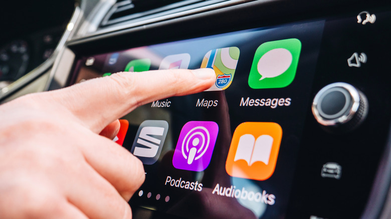 Close-up of a person's hand interacting with the Apple CarPlay touchscreen interface inside a vehicle.