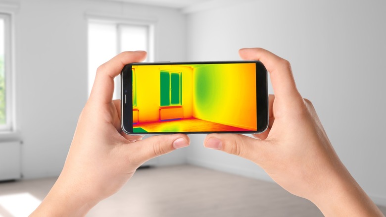 A person using a smartphone thermal camera to inspect a wall for heat leaks.