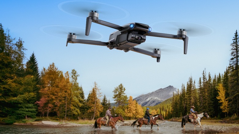 An aerial perspective of three horseback riders crossing a river in a wooded mountain valley.