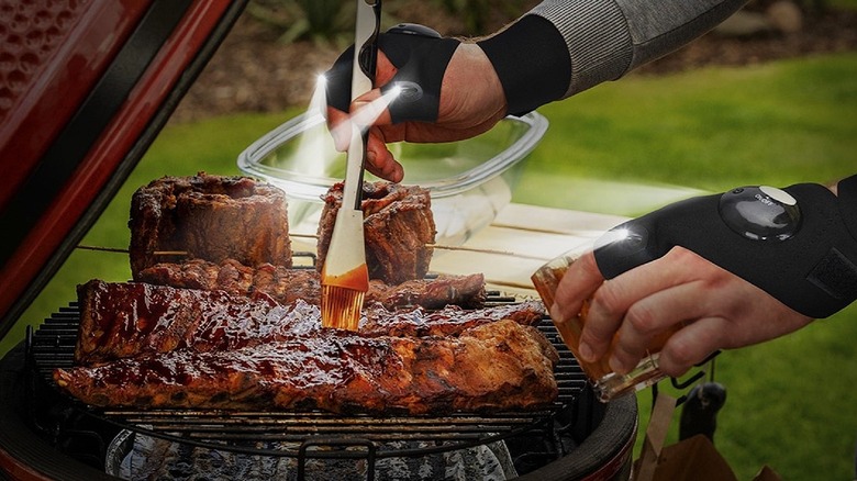 A person using Parigo LED flashlight gloves to illuminate a grill while cooking outdoors at night.