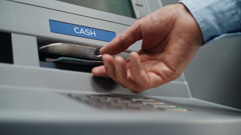 A person using a traditional outdoor ATM in a city environment.