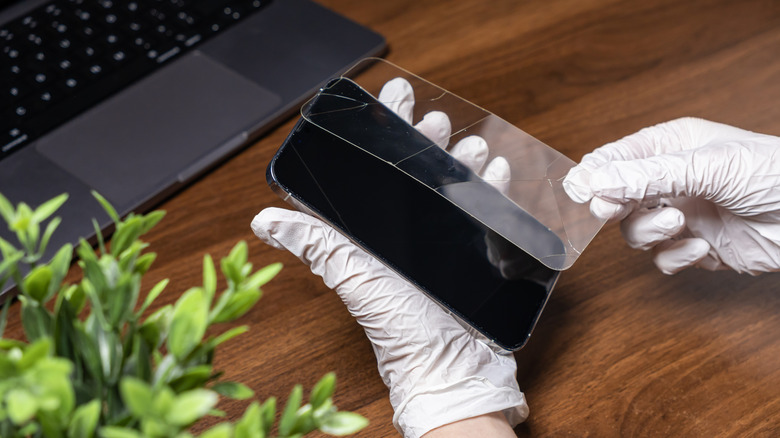 A cracked tempered glass screen protector being carefully removed from a smartphone.