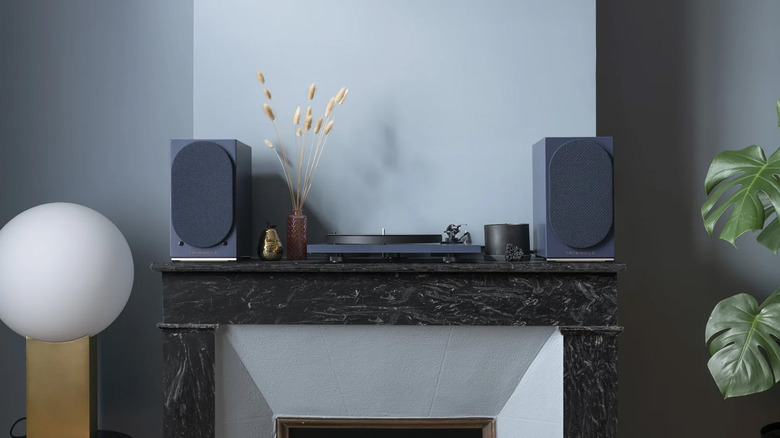 Two Triangle AIO Twin speakers positioned on a wooden mantle above a fireplace.