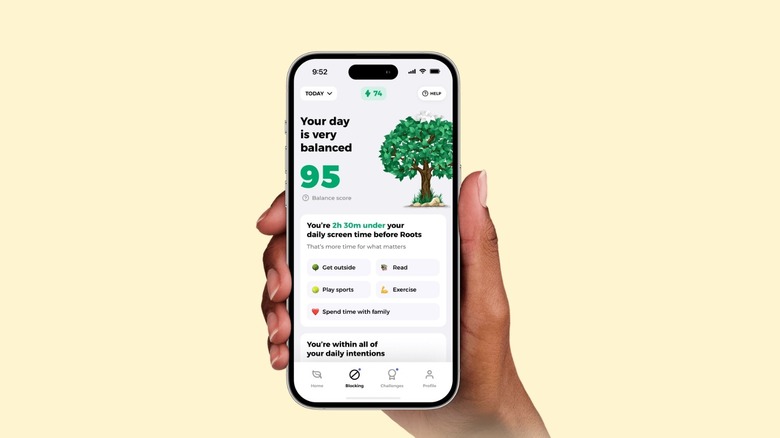 A close-up of a hand holding an iPhone with the Roots digital detox app open on the screen.