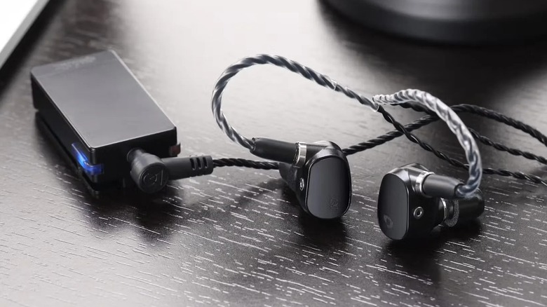 Qudelix-5K DAC resting on a dark table with high-fidelity IEMs.