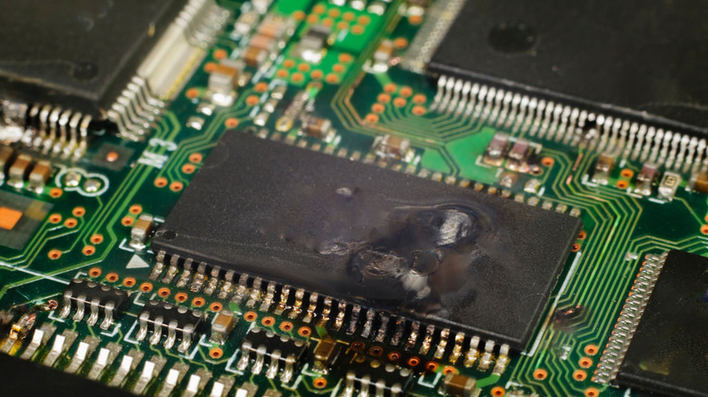A scorched and short-circuited integrated circuit on a computer motherboard.