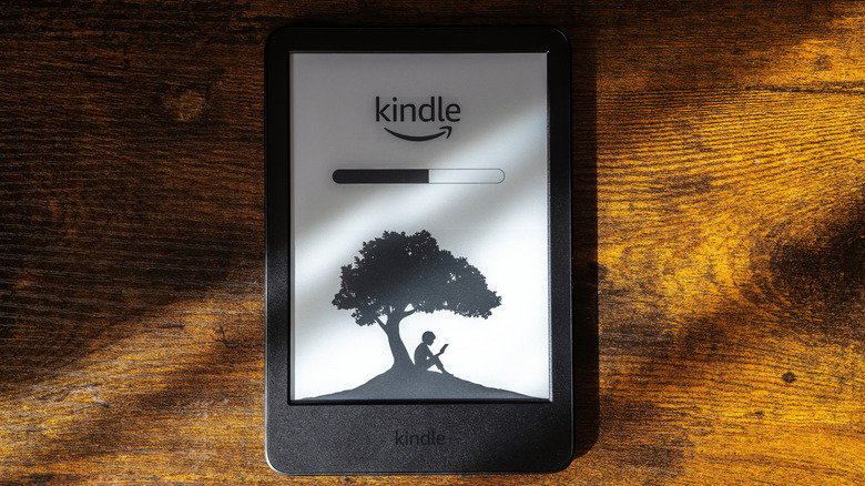 A Kindle e-reader lying flat on a textured wooden table.