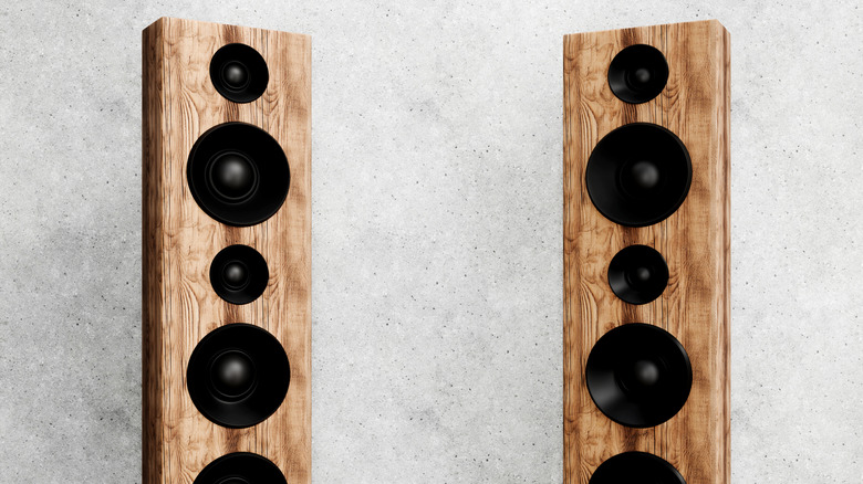 Two floor-standing wooden speakers against a clean wall.