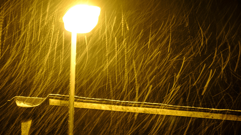 Snow falling through the yellow beam of a street lamp at night.