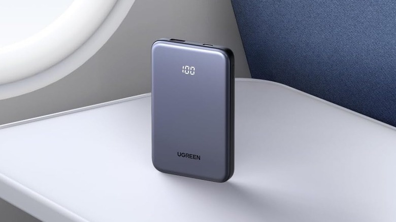 A compact Ugreen Nexode 10K power bank resting on an airplane seat tray table.