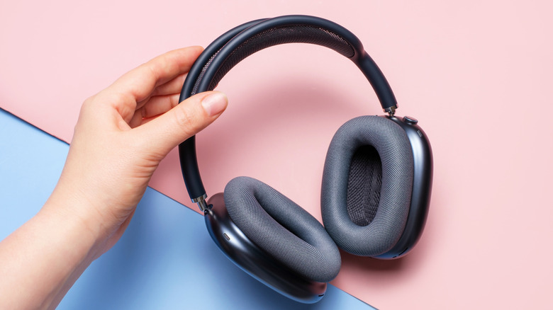 A person holding the AirPods Max against a vibrant pink and blue gradient background.