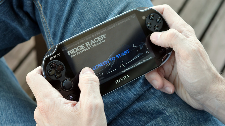 A person playing Ridge Racer on a PlayStation Vita, showing the screen in motion.