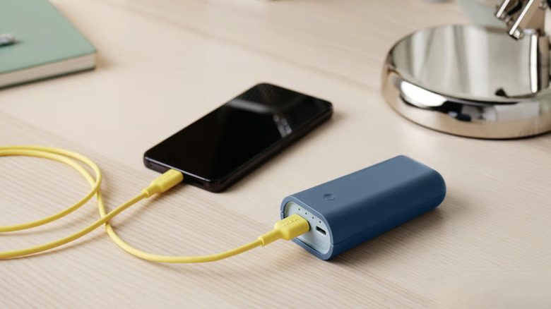 A modern smartphone connected to a compact Varmfront power bank with a charging cable.