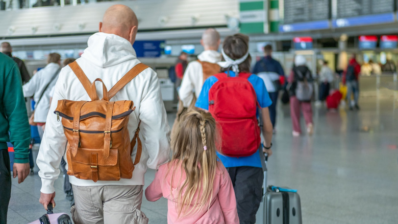 Crowds of travelers walking through a large, modern airport terminal with flight information displays.