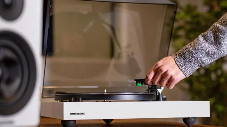 A hand lowers the tonearm onto a Fluance turntable with a clear acrylic dust cover.
