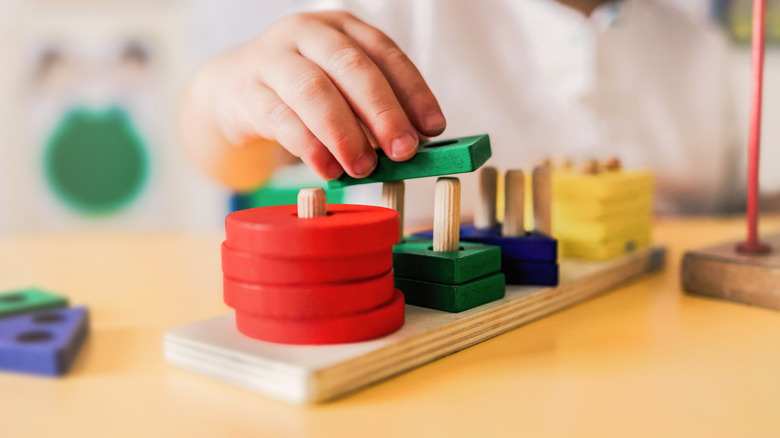 A hand arranging wooden building blocks on a table.