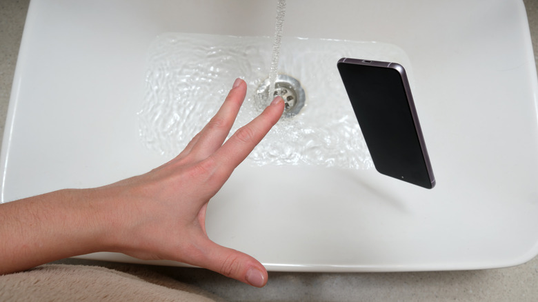 A smartphone being dropped into a sink filled with water.