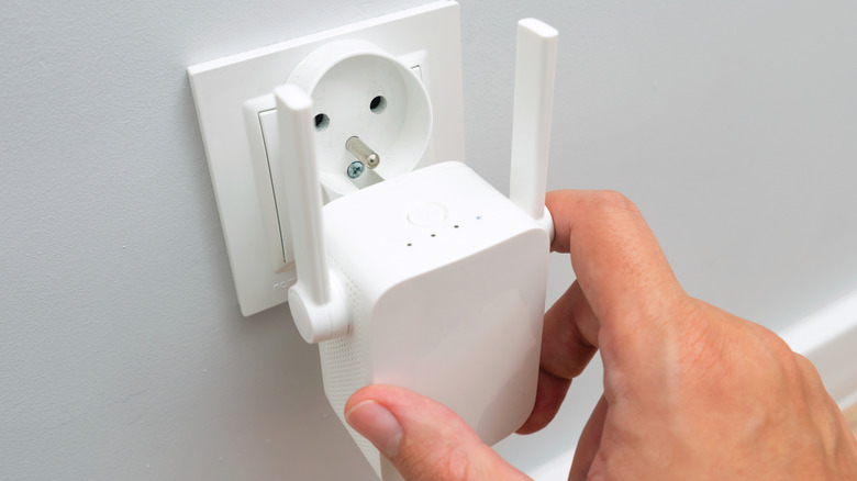A close-up of a person plugging a compact Wi-Fi range extender into a European-style wall power socket.