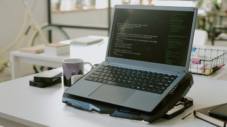 A laptop resting on a cooling pad with visible fans and ventilation.