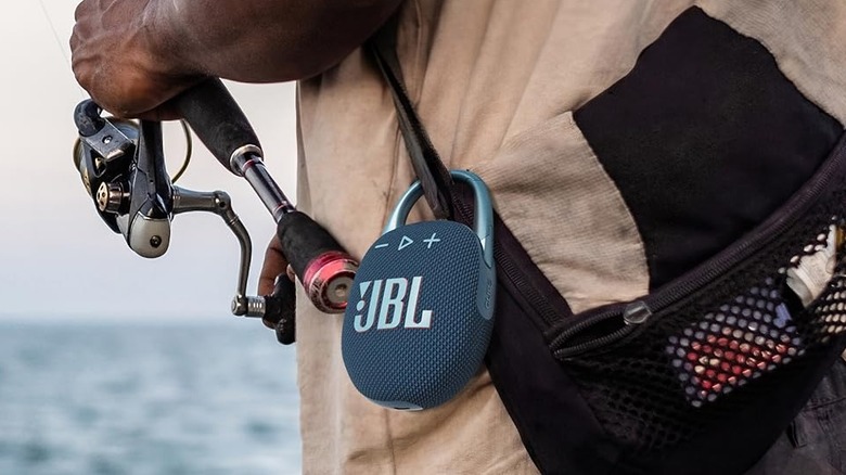 A JBL Clip 5 Bluetooth speaker clipped to the side of a bag during a sunny fishing trip.