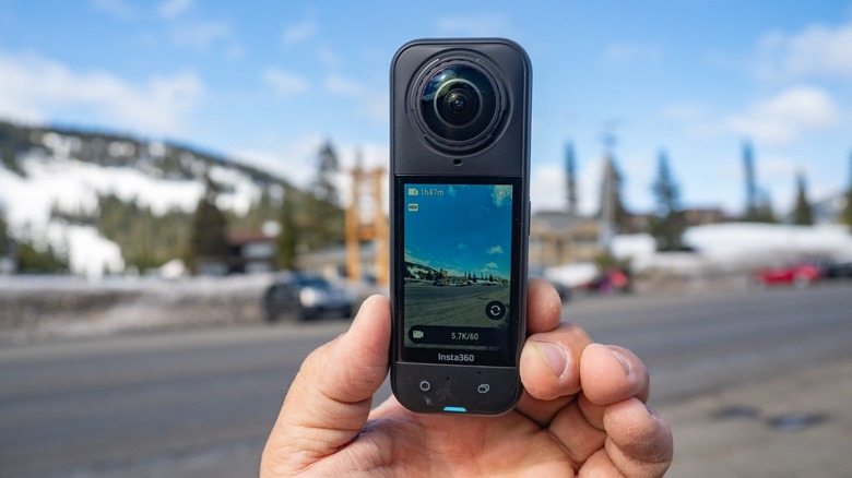 A person holding the Insta360 X5 with a mountain road displayed on its screen.