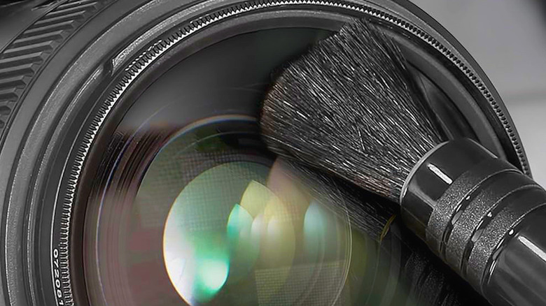 A soft cleaning brush being used delicately on the surface of a camera lens.