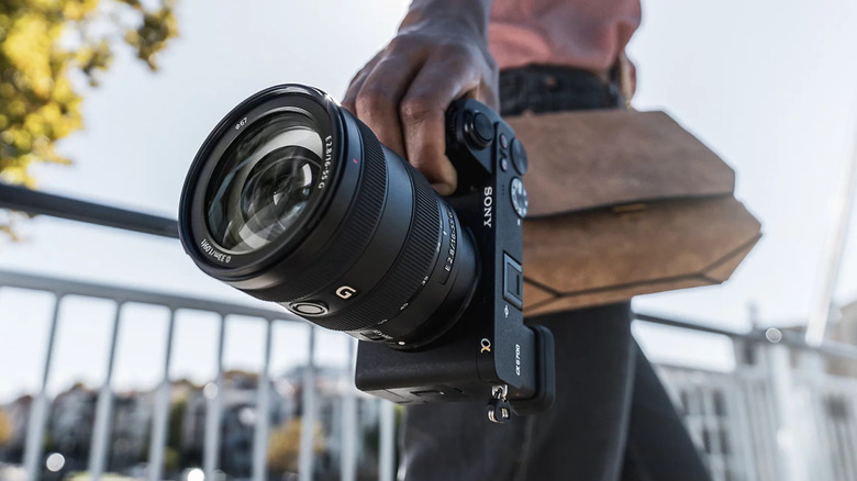 A photographer's hand holding a compact Sony a6700 camera.