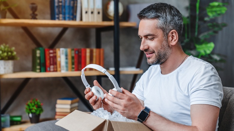 A person holding white headphones while looking at the ear cups.